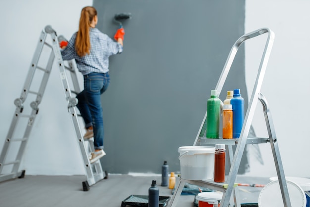 Une femme peintre en bâtiment peint des murs à l'intérieur.