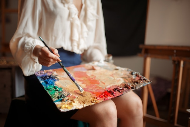 Femme peintre tient la palette de couleurs et le pinceau en studio.