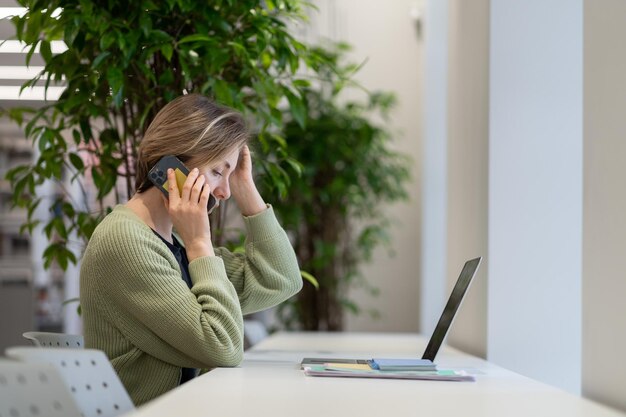 Femme pensive concentrée parlant sur un téléphone portable tout en travaillant à distance dans la salle de lecture de la bibliothèque