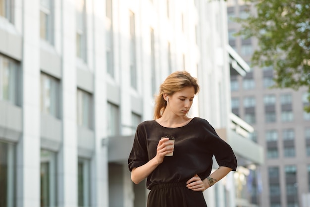 Femme pensive dans le haut gris buvant du café près de l'immeuble de bureaux