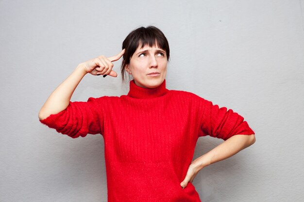 Femme pensive en pull rouge appuya son bâton contre le front sur le mur gris