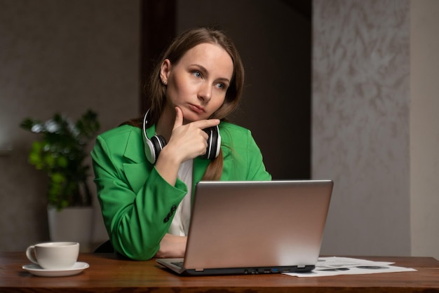 Une femme pensive soupire assise à table près d'un ordinateur portable au bureau