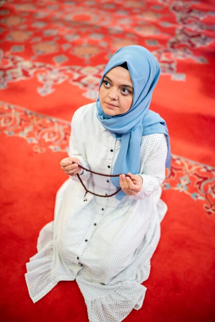 Photo femme avec des perles de prière agenouillée sur le tapis