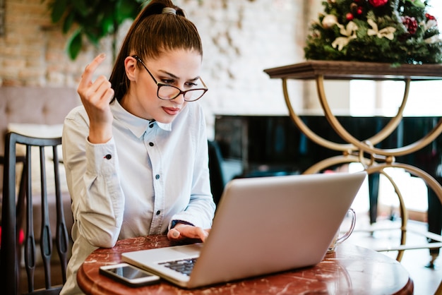 Femme perplexe avec des lunettes en regardant écran d&#39;ordinateur portable.