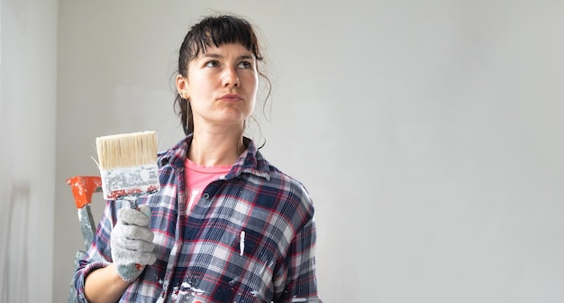 Femme perplexe en rouleau à peinture et peinture blanche pour les murs dans les mains portrait en gros plan Travaux de construction et réparations cosmétiques dans la peinture murale de la maison teinter les travaux de finition de vos propres mains