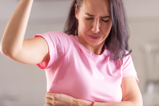 La femme peut se sentir alors qu'elle transpire avec des taches de sueur dans ses aisselles visibles sur un t-shirt rose