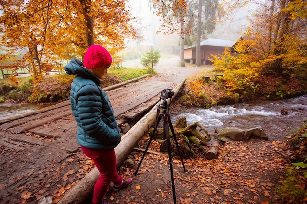 Une femme photographe prend une photo de la cascade de la forêt à l'automne