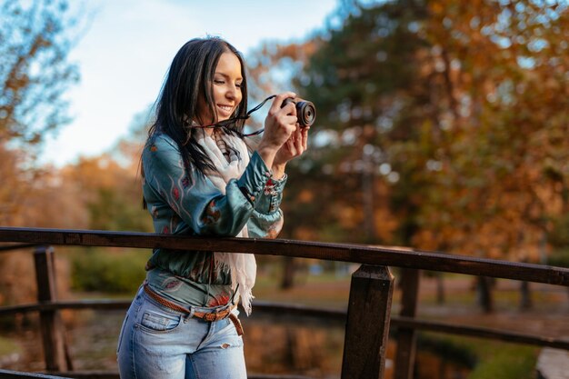 Femme photographe tenant un appareil photo numérique professionnel et prenant des photos sur le pont dans le parc de la ville d'automne.