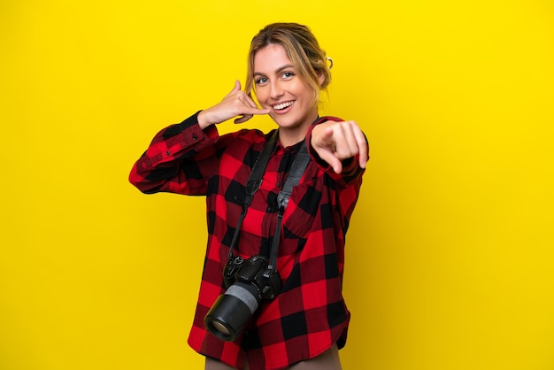 Femme photographe uruguayenne isolée sur fond jaune faisant un geste de téléphone et pointant vers l'avant