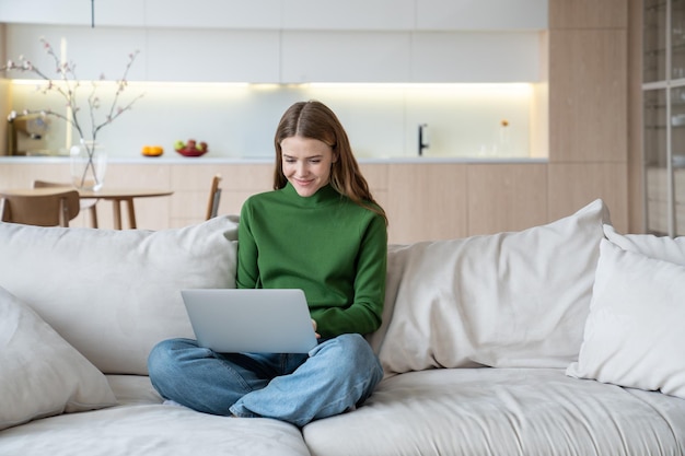 Une femme pigiste travaillant sur un ordinateur portable à genoux, apprenant à distance à la maison, regardant un webinaire