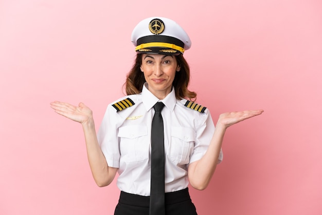 Femme pilote d'âge moyen d'avion isolée sur fond rose avec une expression faciale choquée
