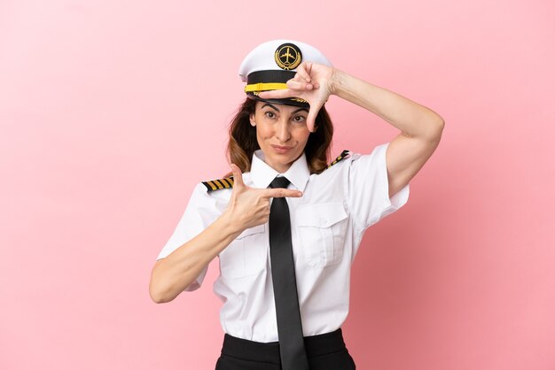 Femme pilote d'âge moyen d'avion isolée sur le visage de focalisation de fond rose. Symbole d'encadrement