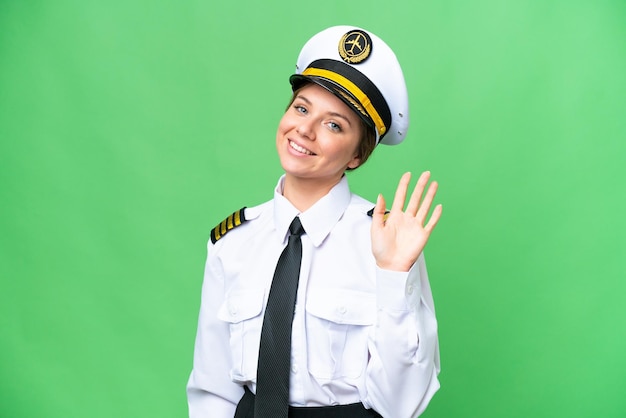 Femme pilote d'avion sur fond isolé chroma key saluant avec la main avec une expression heureuse