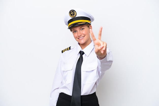 Femme pilote caucasien avion isolé sur fond blanc souriant et montrant le signe de la victoire