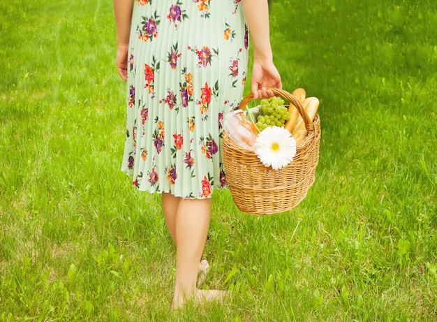 Femme sur le pique-nique se tenir sur l&#39;herbe verte et tient le panier de pique-nique dans une main.