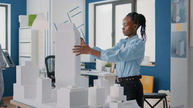 Femme plaçant des plans sur la table pour concevoir le modèle de construction et la disposition de la construction. Architecte utilisant une maquette et un croquis industriel pour créer une structure pour le développement de projets.