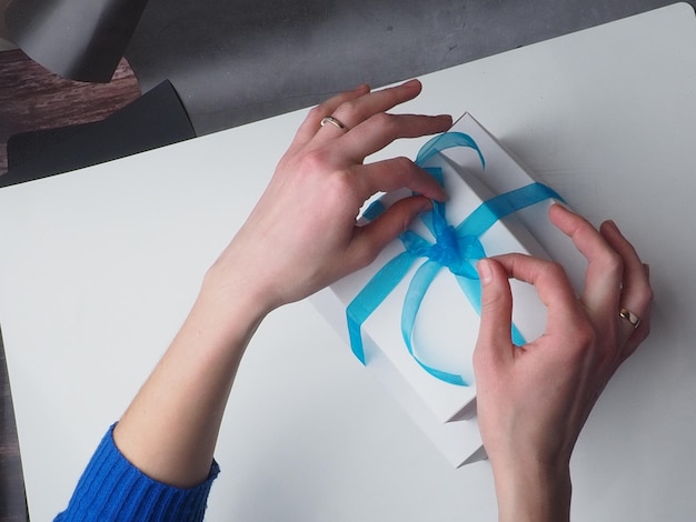 Une femme place un arc bleu sur une boîte blanche avec un ruban bleu.