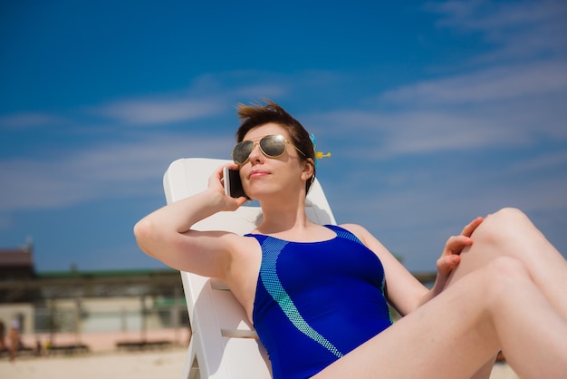 Femme sur la plage en maillot de bain bleu parlant au téléphone
