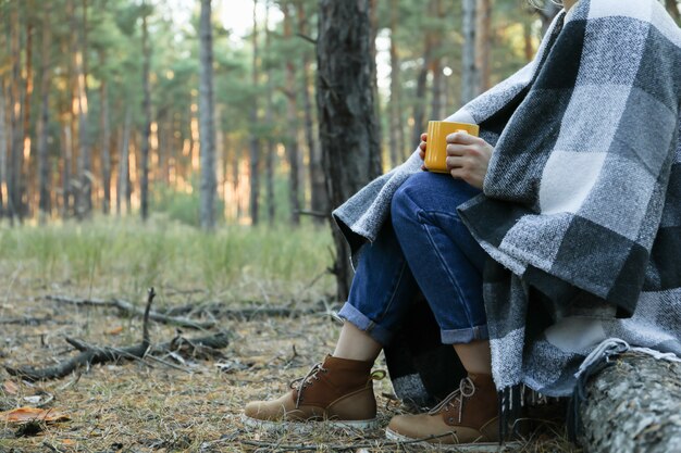 Femme avec plaid et tasse de boisson chaude dans la forêt de pins, espace pour le texte