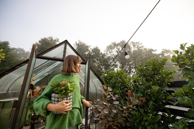 Femme avec des plantes près de serre à l'arrière-cour