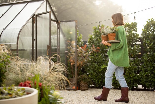 Femme avec des plantes près de serre à l'arrière-cour