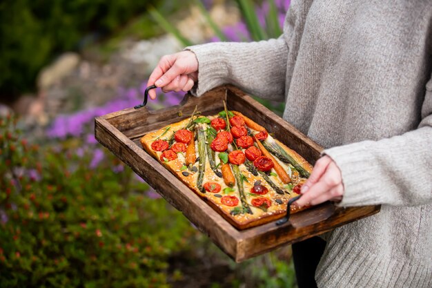 Femme avec un plateau de focaccia dans la cour, avec des fleurs