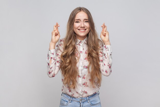 Une femme pleine d'espoir, joyeuse et belle lève les doigts croisés tout en souhaitant avec confiance de gagner.