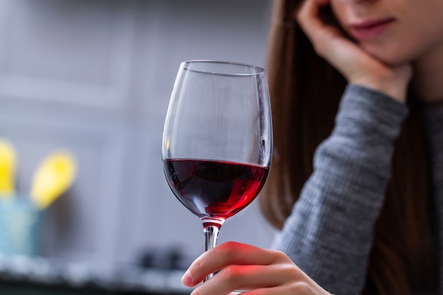 Femme en pleurs déprimée et divorcée, assise seule dans la cuisine de sa maison et buvant un verre de vin rouge à cause de problèmes au travail et de problèmes dans les relations. Problèmes sociaux et de vie