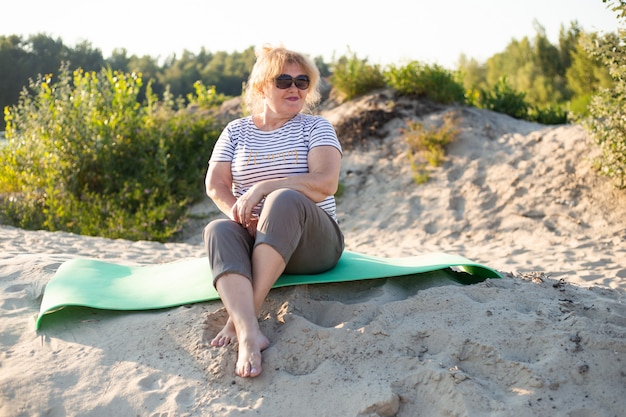 Femme plus âgée assise sur un sable à la plage d'été