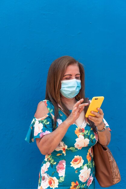 Femme plus âgée avec masque de protection utilisant son téléphone dans la rue.