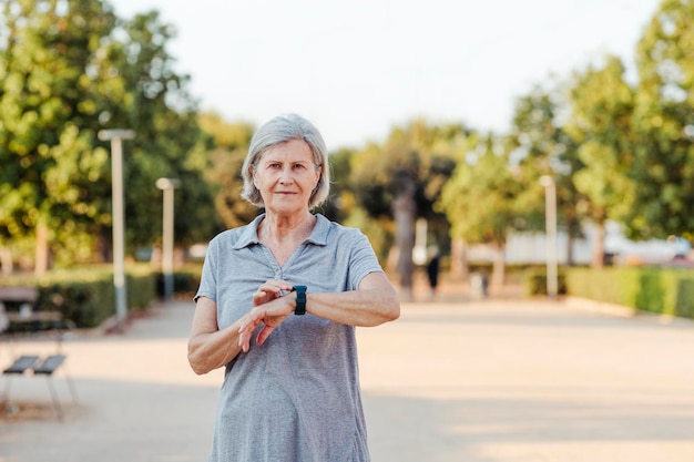 Une femme plus âgée avec une montre de sport se penche sur l'appareil photo dans un parc extérieur