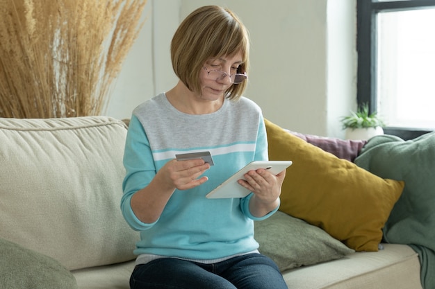 Femme plus âgée, shopping en ligne avec carte de crédit à l'aide de tablette numérique