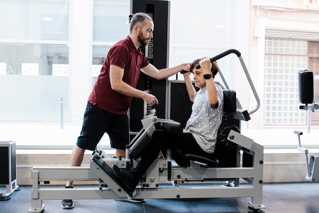 Femme Plus âgée Travaillant Sur Les Machines De La Salle De Sport Avec Son Entraîneur Personnel