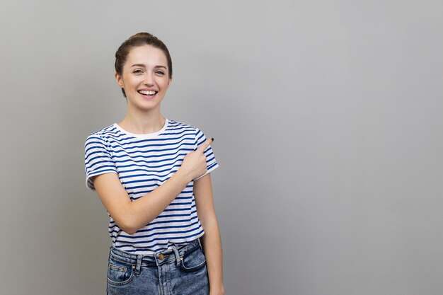 Femme pointant de côté montrant un espace de copie vierge pour la présentation d'idées regardant souriant à la caméra