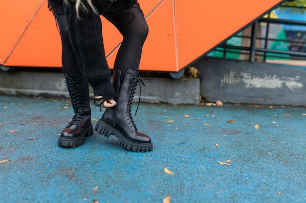 Une femme portant des bottes en cuir noir se tient devant un mur orange.