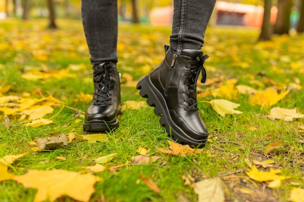 Une femme portant des bottes noires se dresse sur l'herbe en automne.