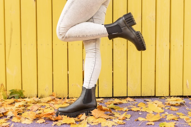 Une femme portant des bottes de pluie noires se tient devant un mur en bois jaune.