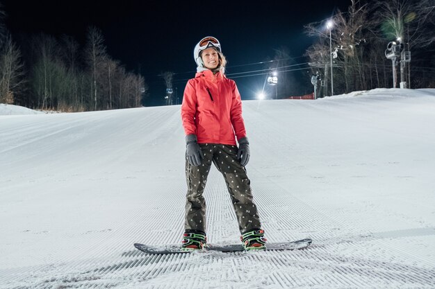 Femme portant un casque avec snowboard sur la piste de ski. Équitation du soir