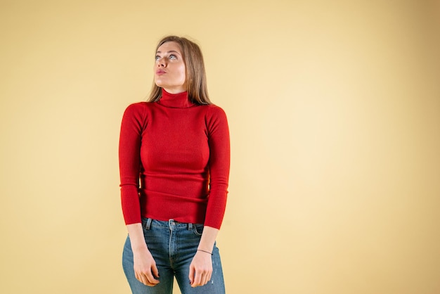 Une femme portant un chandail rouge se dresse sur un fond jaune.