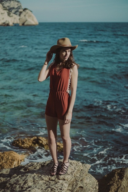 Femme portant un chapeau debout sur un rocher contre la mer