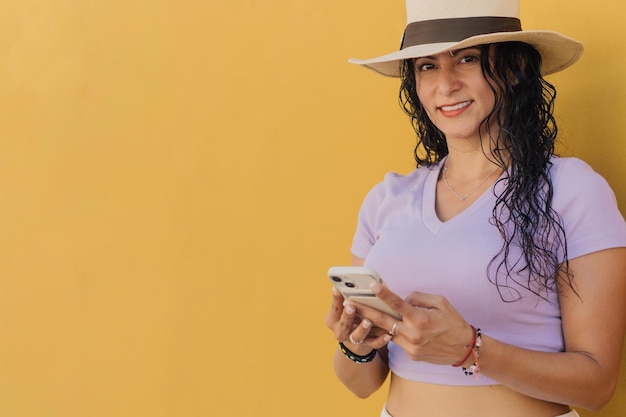 Photo une femme portant un chapeau et un haut violet sourit en utilisant un téléphone.