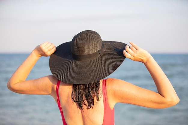 Une femme portant un chapeau à larges bords et un maillot de bain regarde la mer