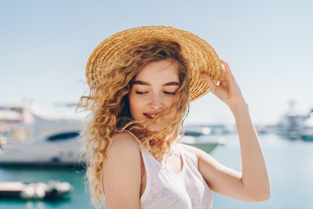 Une femme portant un chapeau de paille se tient sur une jetée devant un yacht.