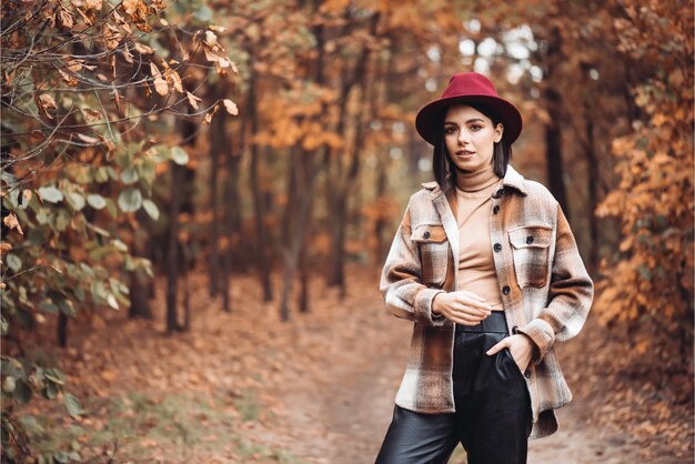 Une femme portant un chapeau rouge et une veste à carreaux se tient dans les bois.