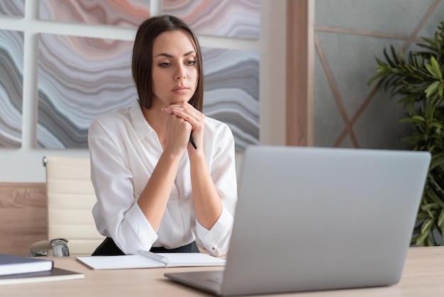 Femme portant une chemise blanche assis Table avec ordinateur portable et cahier prenant des notes Concept de travail