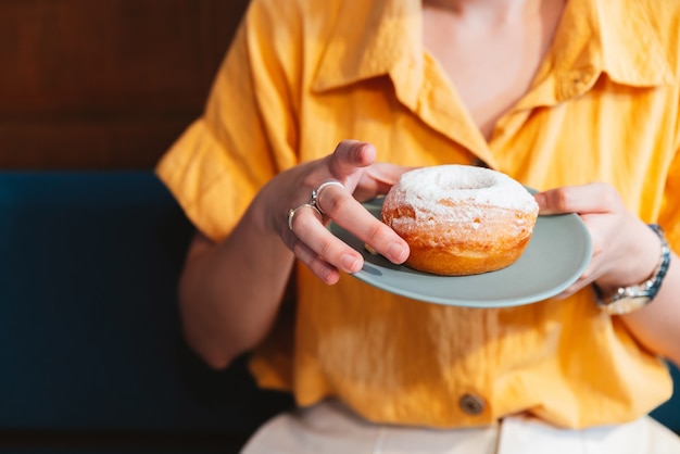 Femme portant une chemise jaune tenant et montrant une assiette vert pâle de beignet glacé au sucre.