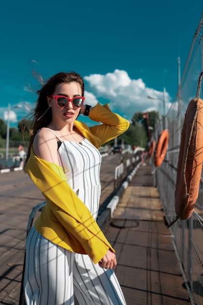 Une femme portant un chemisier jaune et des lunettes profitant du beau temps ensoleillé tout en marchant