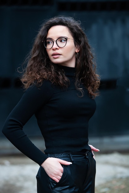 Une femme portant un col roulé noir et des lunettes se tient devant un mur noir.