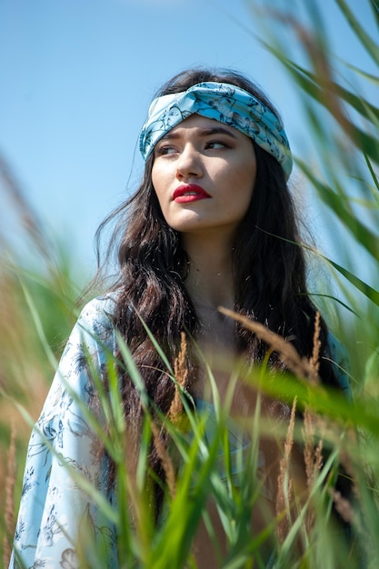 Une femme portant une écharpe bleue est assise dans un champ d'herbes hautes.