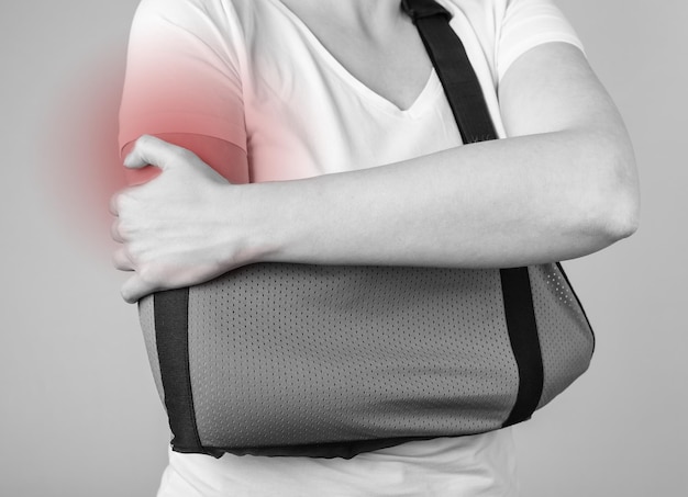 Femme portant une écharpe pour soutenir l'épaule blessée avec une tache rouge Blessure traumatique au bras Fracture de l'acromion Concept de soins de santé Dispositif médical pour la réduction de la douleur et l'immobilisation Noir et blanc